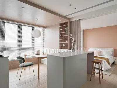 A modern, minimalist kitchen with white countertops, wooden chairs, and a white pendant light hanging from the ceiling.