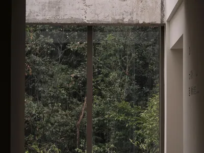 An industrial-style living room with a brown fabric armchair, metal frame, and glass window overlooking a forest.