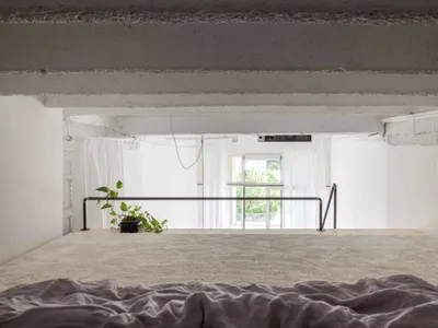 A minimalist bedroom with concrete walls, floor-to-ceiling windows, and a minimalist bed platform.