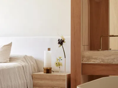 A minimalist bedroom with white walls, a white bed, a marble nightstand, and a vase with flowers.