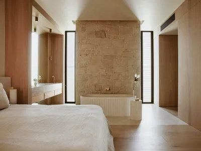 A minimalist bedroom with a large bed, a wooden floor, and a white plaster wall in the center.