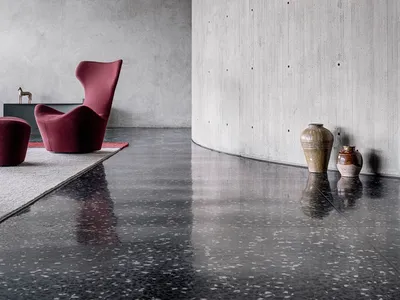 A minimalist living room with concrete walls, a red armchair, and terrazzo flooring.