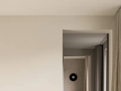 A minimalist bedroom with neutral tones, featuring a white wall, beige curtains, and a simple wooden stool.