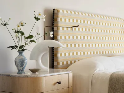 Bedroom with minimalist design featuring a wooden nightstand with a marble top, a bed with a striped fabric headboard, and fl