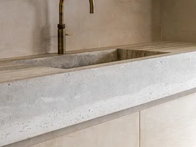 Modern minimalist kitchen featuring a concrete countertop and brushed gold faucet.