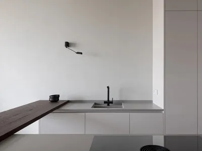 A minimalist modern kitchen featuring concrete countertops, stone backsplash, and a mixer sink.