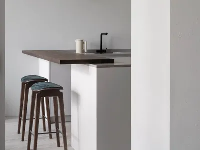 Modern kitchen featuring wooden stools, concrete countertop, and metal faucet.