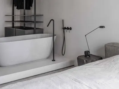 Minimalist bedroom featuring a concrete wall and floor, with a freestanding bathtub and black minimalist wardrobe system.
