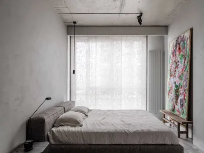 Modern minimalist bedroom with a textured concrete ceiling, large window with sheer curtains, and an abstract painting leanin