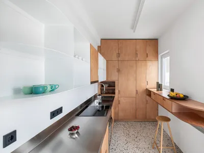 A minimalist residential kitchen with wooden cabinets, stainless steel countertops, and a small dining nook.