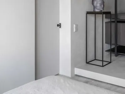 A minimalist bedroom featuring a concrete wall and floor, with a bed and a sculpture on a pedestal.