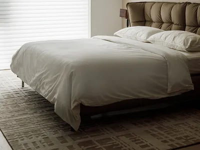 A modern bedroom with a brown leather bed, white blinds covering a window, and a white blanket on the bed.