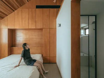 A minimalist bedroom with wooden walls and floor, featuring a bed and a small bathroom with a bathtub.