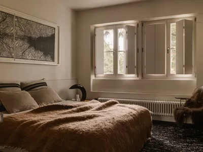 Neutral-toned minimalist bedroom with a bed, window, and chair.