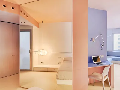 Minimalist bedroom with pink and white walls, a bed, and a desk with a laptop.