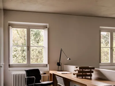 A minimalist home office featuring a wooden counter with a lamp and a black office chair.