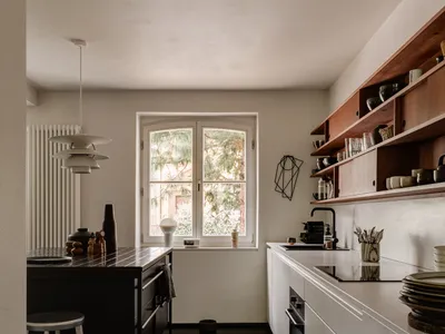 Modern minimalist kitchen with white cabinetry and wooden accents, featuring an island with pendant lighting and open shelvin