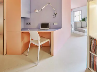 A modern home office featuring a desk with a laptop and lamp, surrounded by pastel-colored walls.