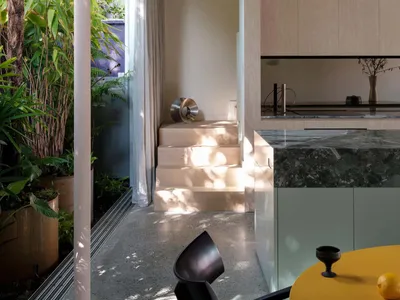 A modern living, dining, and kitchen area featuring concrete, marble, and wood materials.