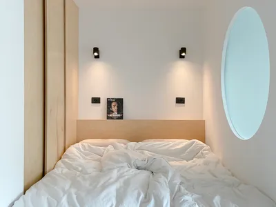 A minimalist bedroom with white walls, a wooden bed frame, and white towels.
