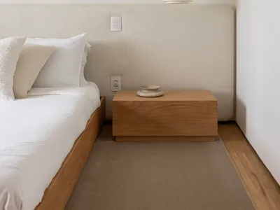 Modern minimalist bedroom featuring a wooden bed with a fabric headboard, pendant light, and minimalistic decor.