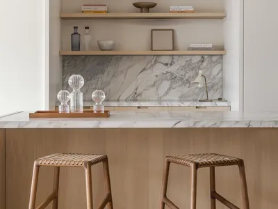 A modern kitchen with white marble countertops and wooden stools.