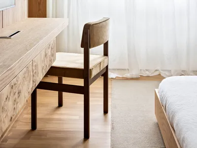 A modern minimalist bedroom with a wooden floor, a white bed with a light brown wooden frame, and a desk with a television.