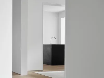 A modern minimalist kitchen with white cabinets and a white island, featuring wooden stools and a black backsplash.
