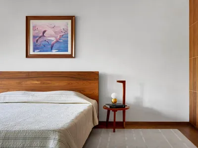 A modern minimalist bedroom featuring wooden furniture and a textured white bedspread.