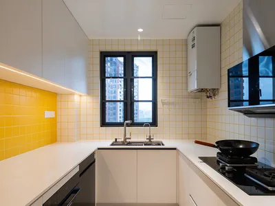 Modern kitchen with yellow tile backsplash and white countertops, featuring a black range hood and stainless steel appliances
