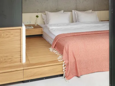 A minimalist bedroom featuring a wooden bed frame with a concrete wall and wooden ceiling.