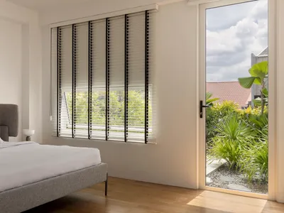 A minimalist bedroom featuring a bed with white sheets, a gray upholstered headboard, and a window with white mini blinds and