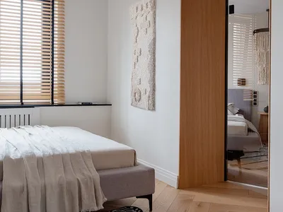 A minimalist bedroom featuring a bed with light wood frame and white bedding, surrounded by light wood floors and walls, and