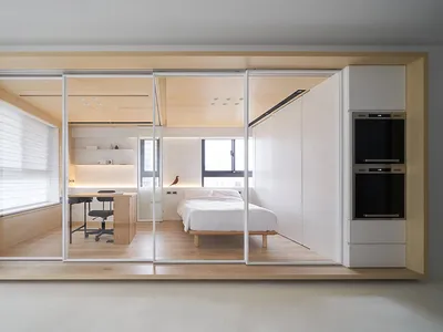 Modern minimalist bedroom featuring a white bed with wooden walls and furniture.