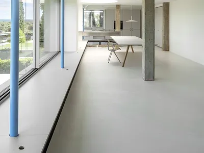 Modern minimalist living room with concrete walls and floor, large windows, and simple furniture.