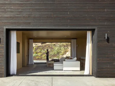 A modern living room with white furniture and a view of a rocky hillside.
