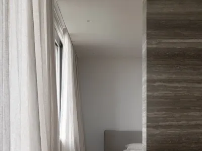 Interior shot of a minimalist bedroom featuring concrete walls, wooden flooring, and a bed with a simple headboard and white