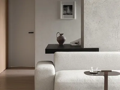 A minimalist living room with concrete walls, a white sofa, and a coffee table with a glass cup.