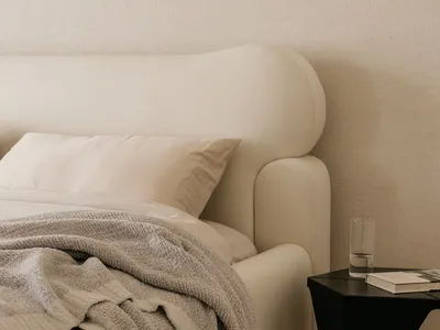 A minimalist bedroom with a white bed, grey blanket, and black side table.