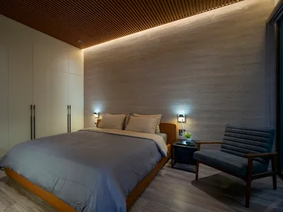 Minimalist bedroom with wood accents, including a textured wall, wood floors, and a wooden chair.