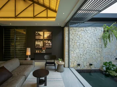A contemporary living room featuring concrete and stone materials, with a dark sofa, wooden table, and artistic wall decor.