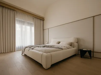 A minimalist bedroom with a neutral-toned bed featuring soft textiles and a modern side table.