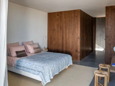 Modern minimalist bedroom with wooden walls, pink bedding, and a blue rug.