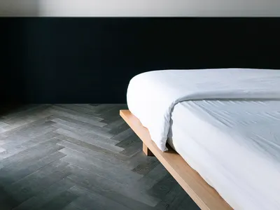 A modern minimalist bedroom featuring a wood platform bed with white bedding against a black and white color block wall.