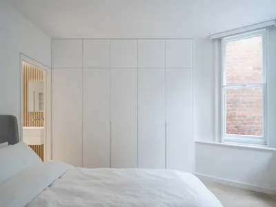 A minimalist bedroom with a white bed and a large white wardrobe.