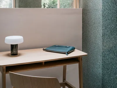 A modern home office featuring a sleek desk, a minimalist lamp, and a leather notebook against a concrete backdrop.
