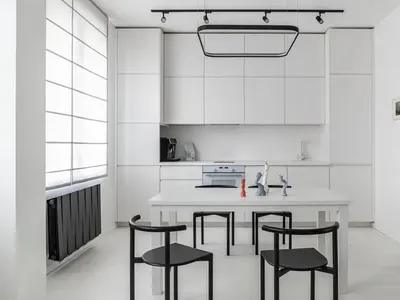 Modern minimalist kitchen featuring white cabinets, a white dining table, and black furniture.