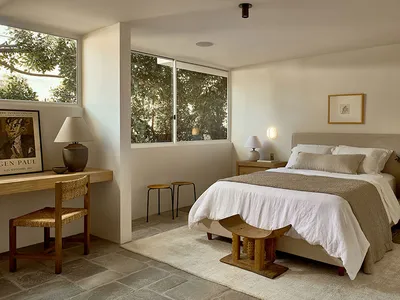 The bedroom features a modern minimalistic design with a wooden bedframe and lamp, complemented by a white rug and a large wi