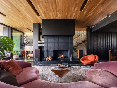 A spacious, industrial-style living room featuring a prominent, modern fireplace made of black slate tiles, surrounded by pin