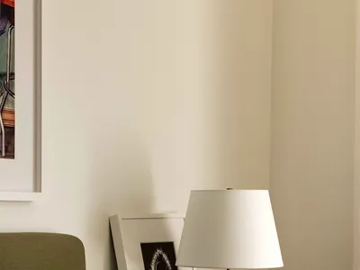A minimalist bedroom featuring a green nightstand with a white lamp, framed artwork, and a small plant.